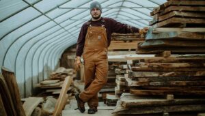Carhartt Latzhose Schreinerei. Vor einem Stabel Holzlatten