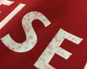 Beispiel für fehlerhaften Textildruck mit Durchbluten-Effekt auf rotem T-Shirt