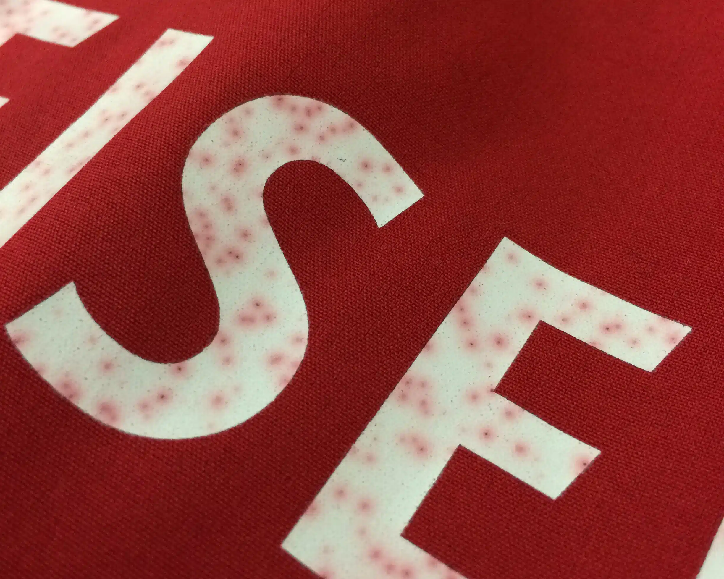 Beispiel für fehlerhaften Textildruck mit Durchbluten-Effekt auf rotem T-Shirt