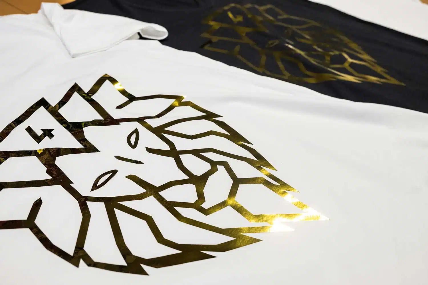 Hochwertiger Textildruck mit Goldfolie-Veredelung auf weißem und schwarzem T-Shirt mit geometrischem Löwen-Design