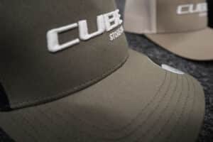 Khakifarbene Cap mit weißem, erhaben gesticktem CUBE-Logo – Beispiel für Logo-Stickerei auf Arbeitskleidung.